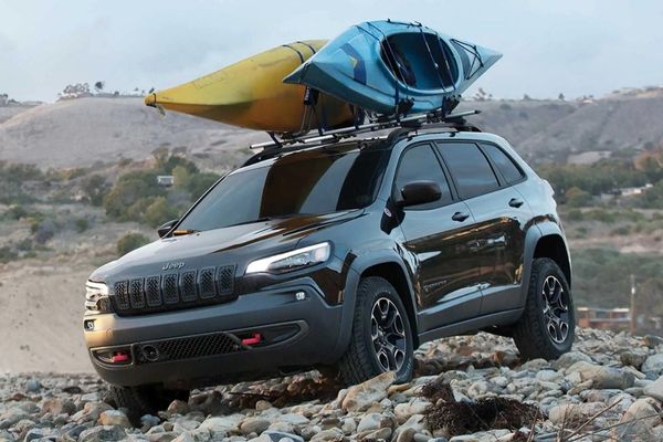 Black Jeep Cherokee driving over rocks with kayaks on its roof