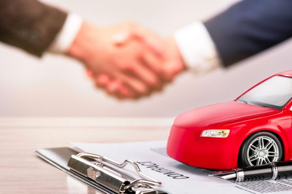 red car with pen and men shaking hands behind paperwork